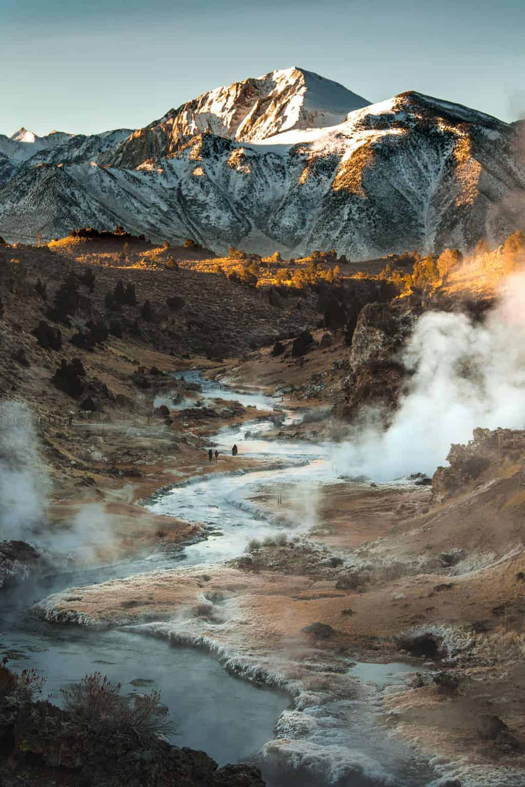 Snow capped mountains with a steaming geothermal river in the foreground.  
