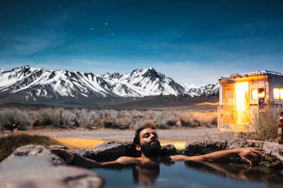 Man soaking in a natural hot spring in Mammoth Lakes at night with mountains in the background. 