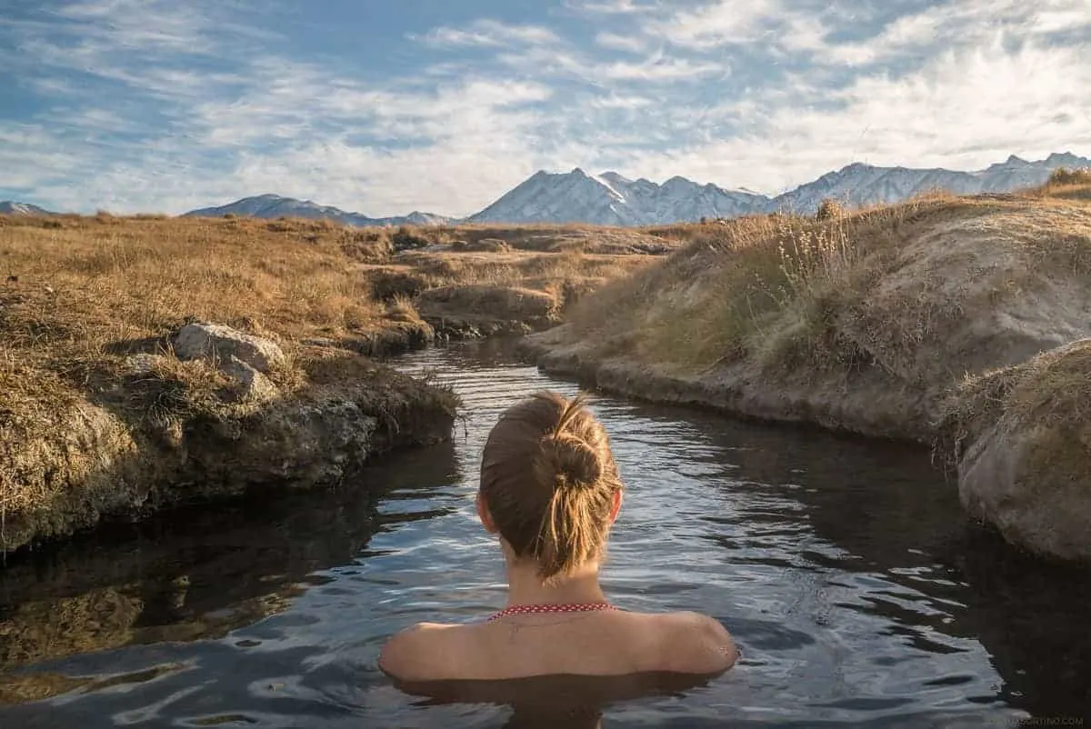 Girl sitting alone in a hot spring in a meadow with mountains in the distance. 