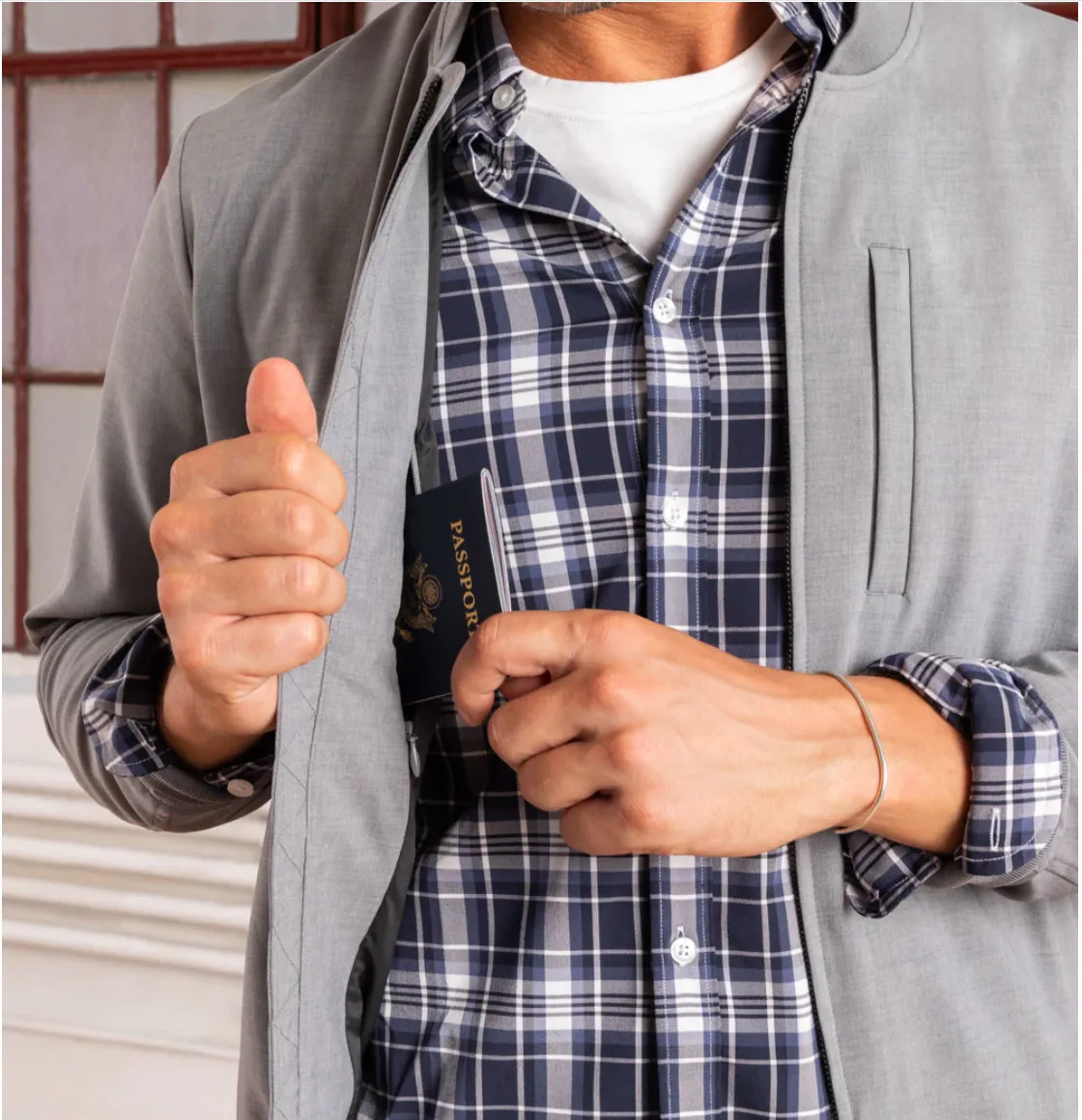 A man in a check shirt putting a passport in an inside pocket of a grey jacket. 