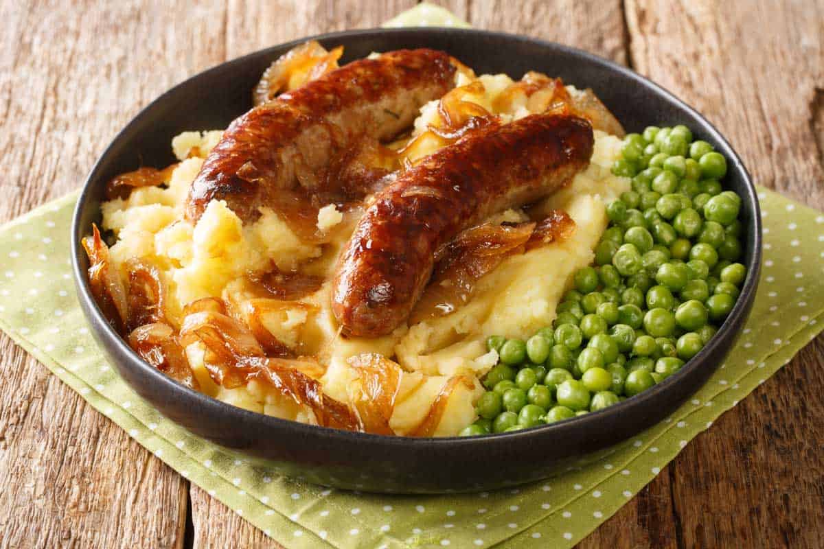 Plate of sausages and mash with peas and gravy. 