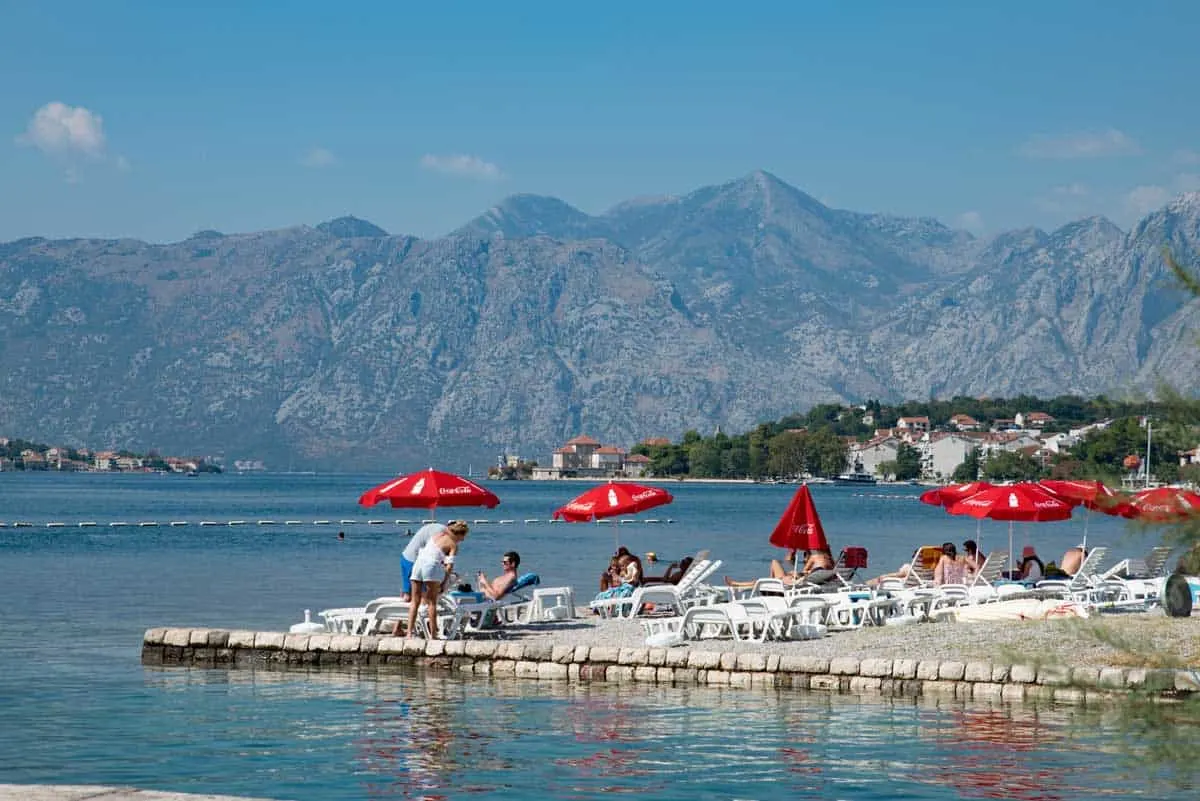 People on sunlounges with red umbrellas on the shore of Bay of Kotor Montenegro.