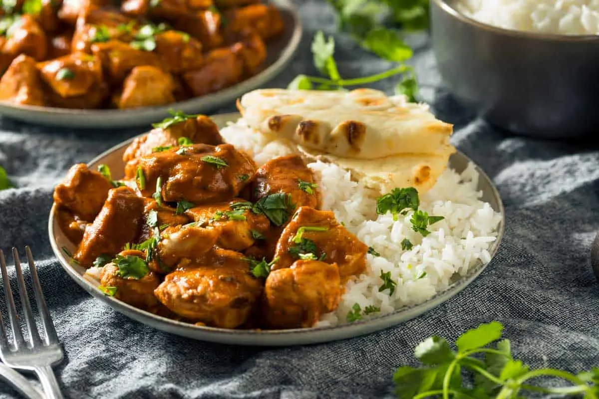 Plate of chicken curry with rice and naan bread. 