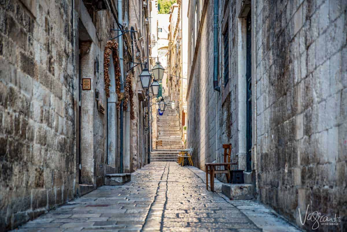 A narrow, empty side street in Dubrovnik Old Town with the iconic steep stairs at the end.