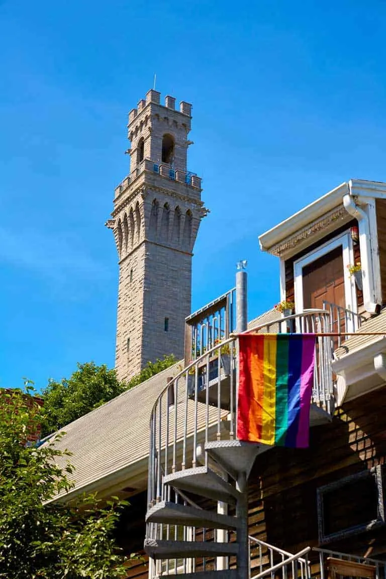 The Pilgrim monument tower in Provincetown Cape Cod with a LGBTQ flag on a balcony in the foreground.