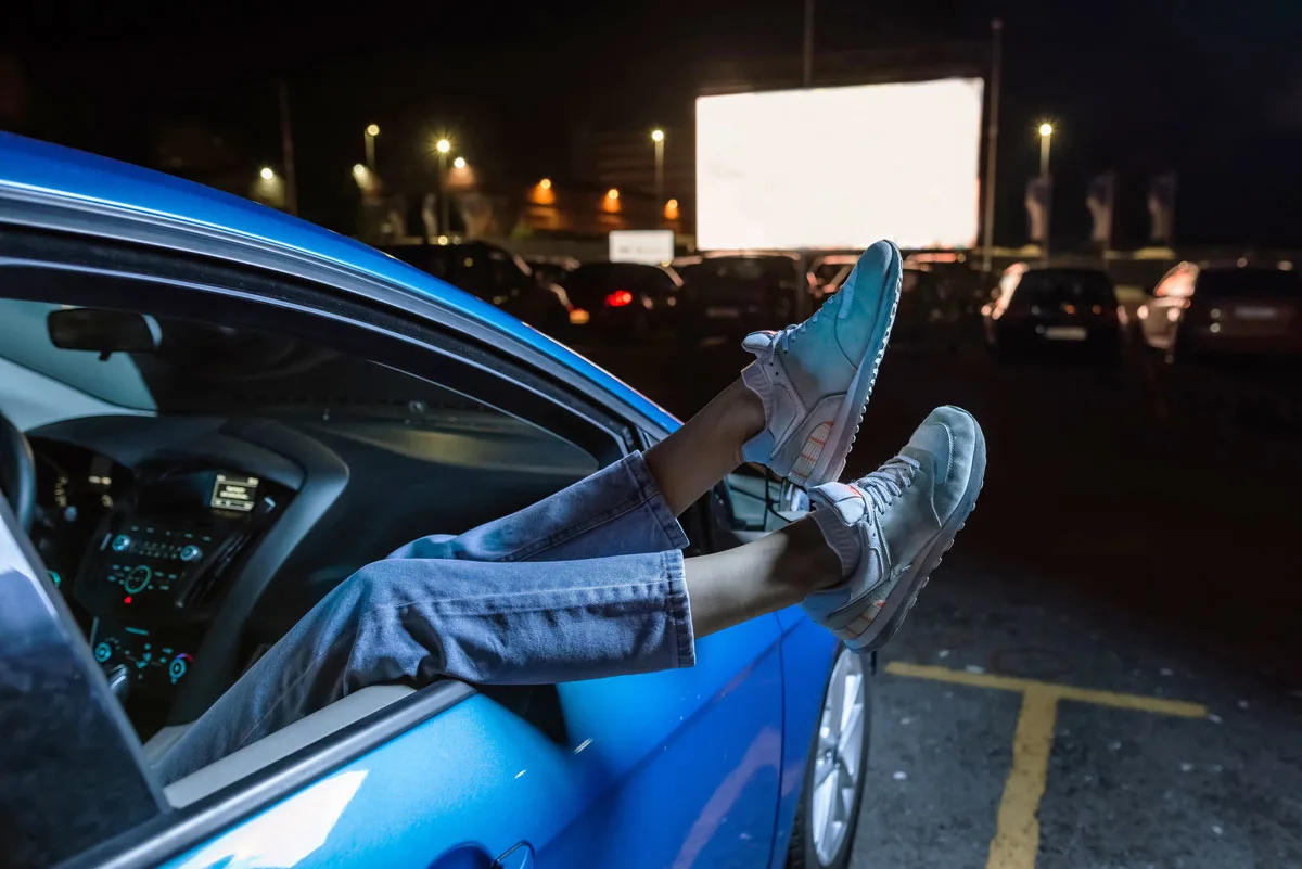 Feet hanging out of a car window at a drive in movie. 