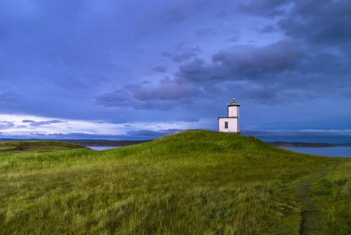 Lighthouse against a blue dusk sky and bright grass meadow in the foreground.