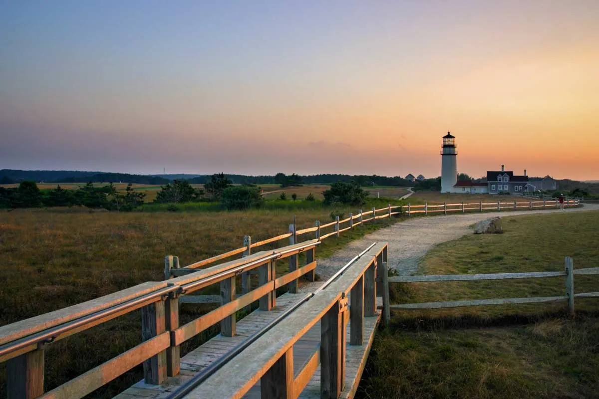 Race Point lighthouse at sunset with fields and boardwalk in the foreground.