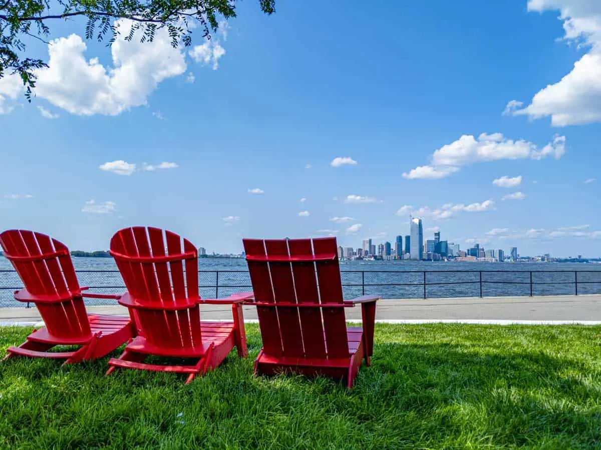 Red wooden deck chairs on a green lawn over looking the New York Skyline.