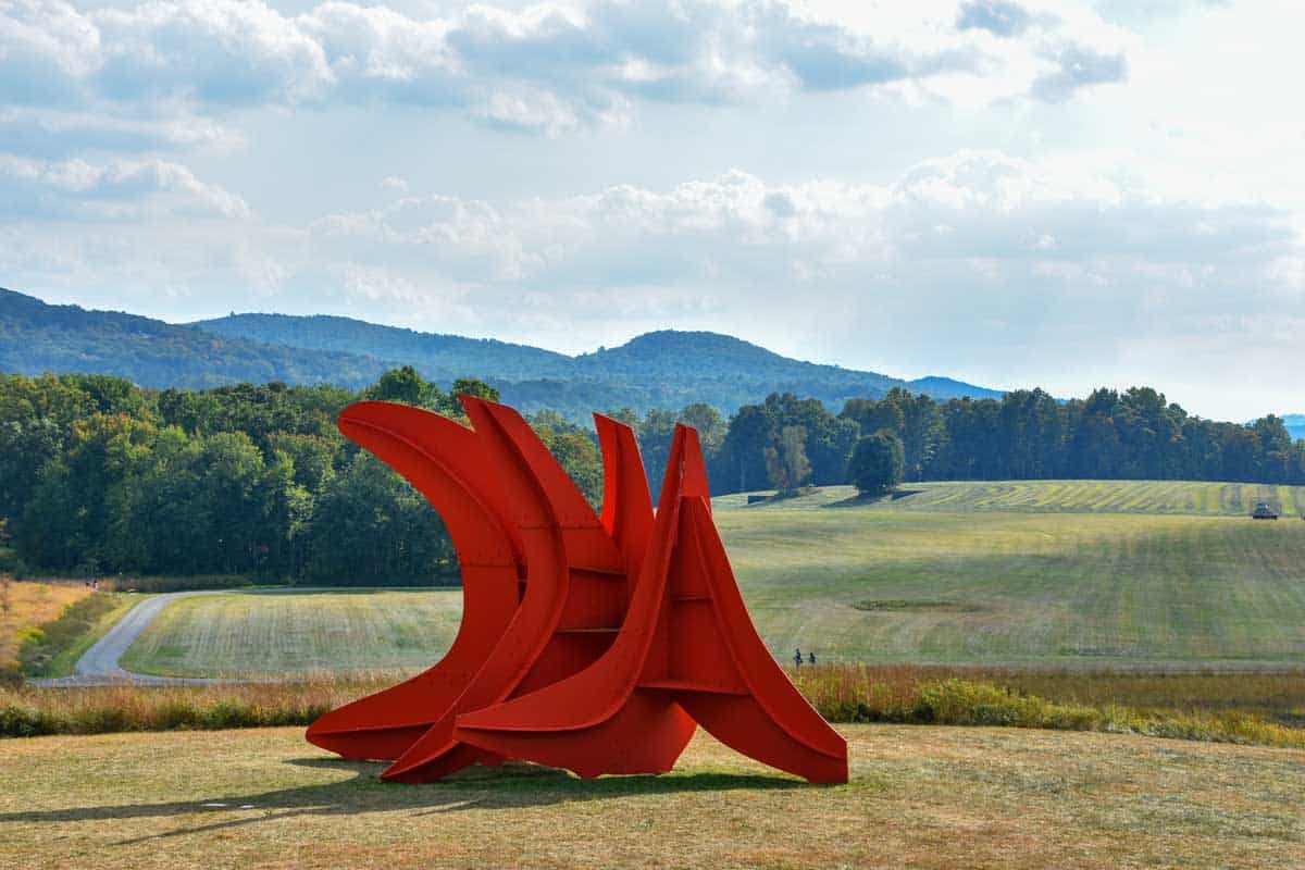 Large red abstract sculpture in a field.