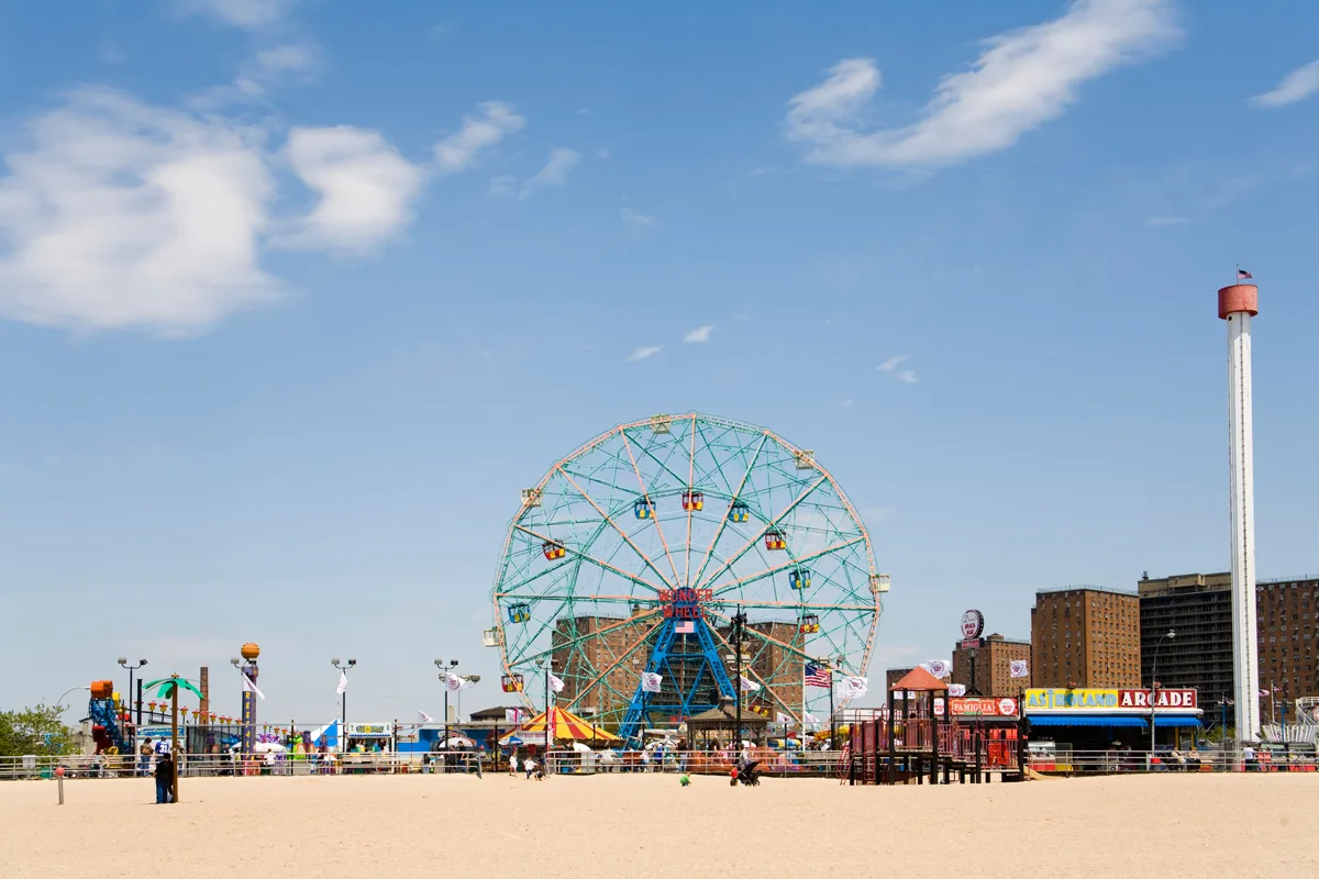 White beach with ferris wheel on a sunny day on Coney Island. 