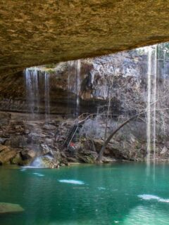 Behind the waterfall at Hamilton Pool Preserve with clear blue swimming hole.