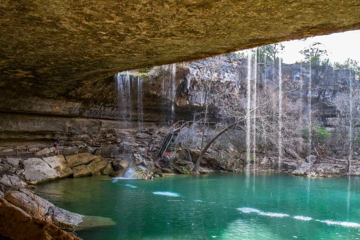 Behind the waterfall at Hamilton Pool Preserve with clear blue swimming hole.
