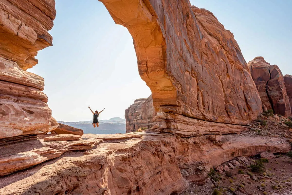 Girl leaping in the air under a red rock arch in Moab Utah.