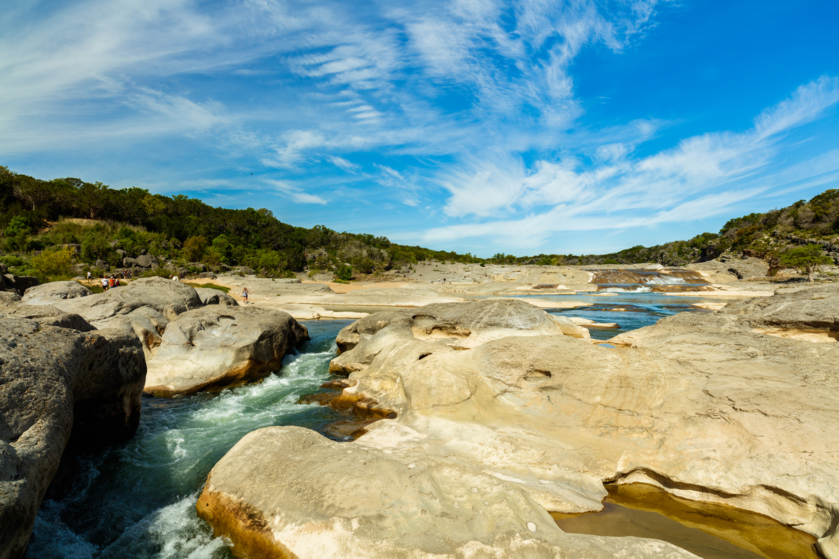 Visitors enjoying the natural beauty of the blue water and bright sandstone river rocks of the Pedernales Falls in the Texas Hill Country on a sunny day.