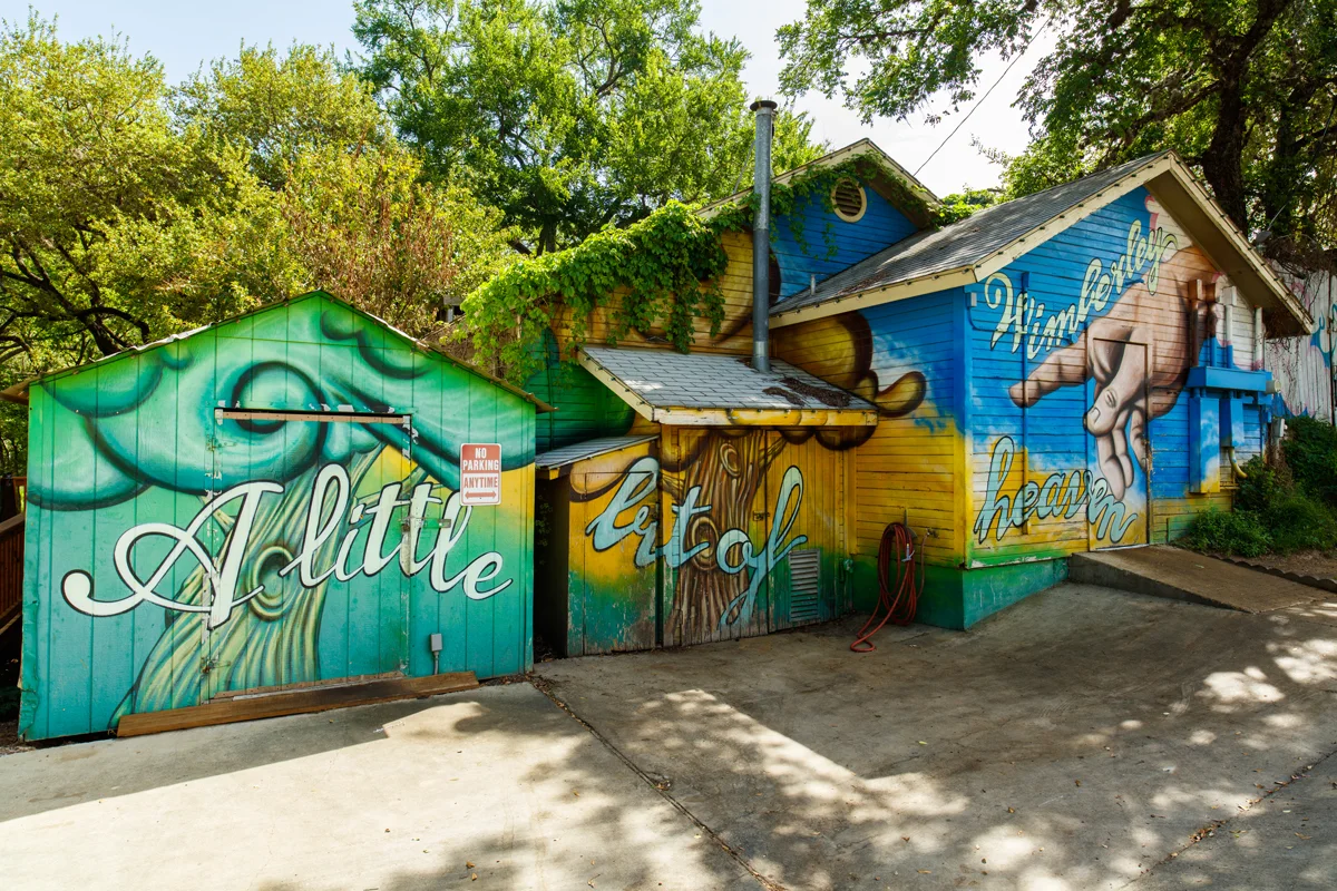 Weatherboard houses painted with murals in blue, green and yellow saying "A little bit of Wimberley Heaven" in Texas. 