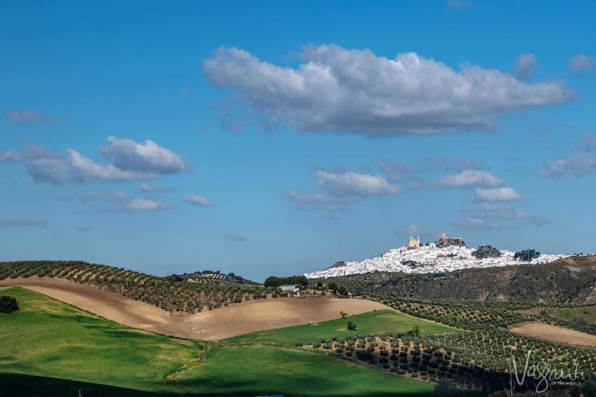 White village in Spain on top of a hill with green meadows in the foreground.