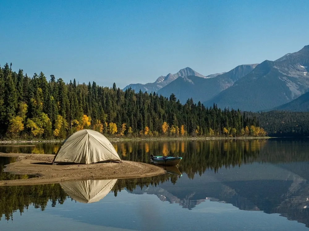 small tent on the banks of a lake reflected in the water.