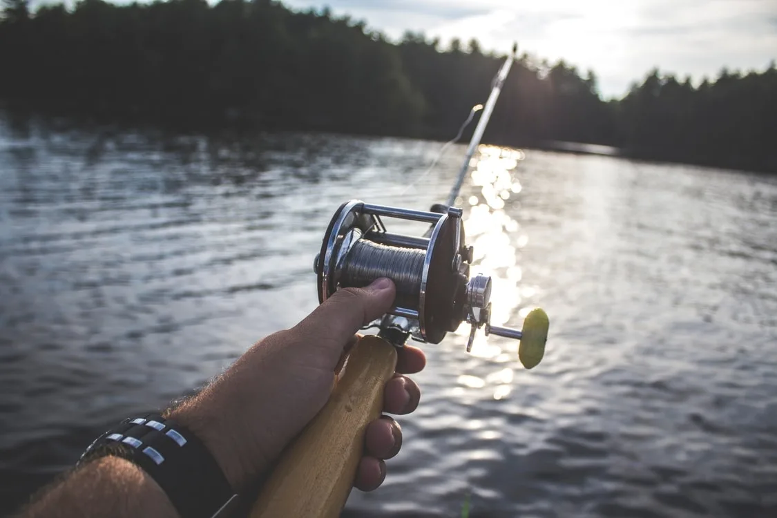 Hand holding a fishing rod over the water at sunset.