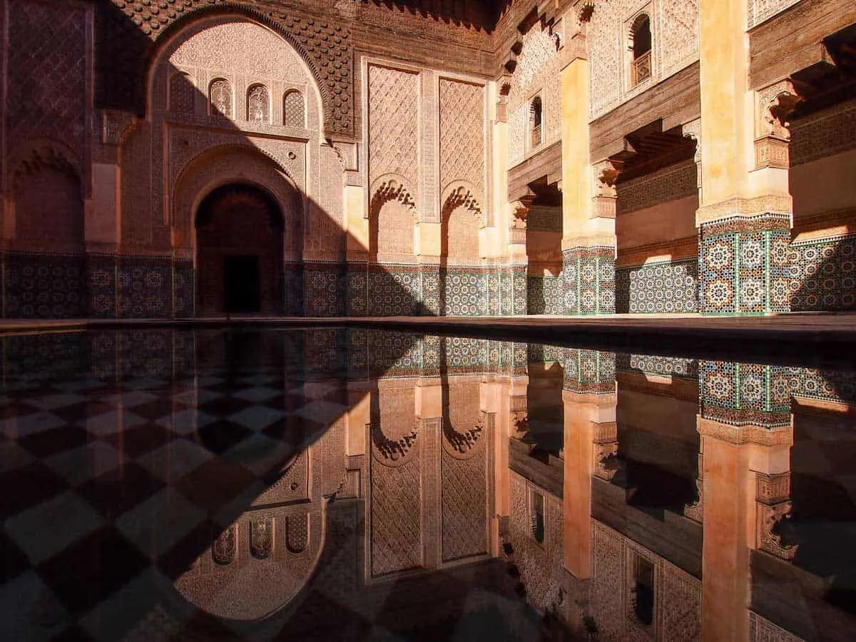 Ben Yousef Medersa in Marrakech with shadow across the pond and tile facade.