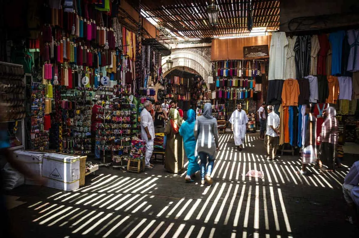 People walking thriugh the shadowy souks of Marrakech.