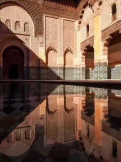 Ben Yousef Medersa in Marrakech with shadow across the pond and tile facade.