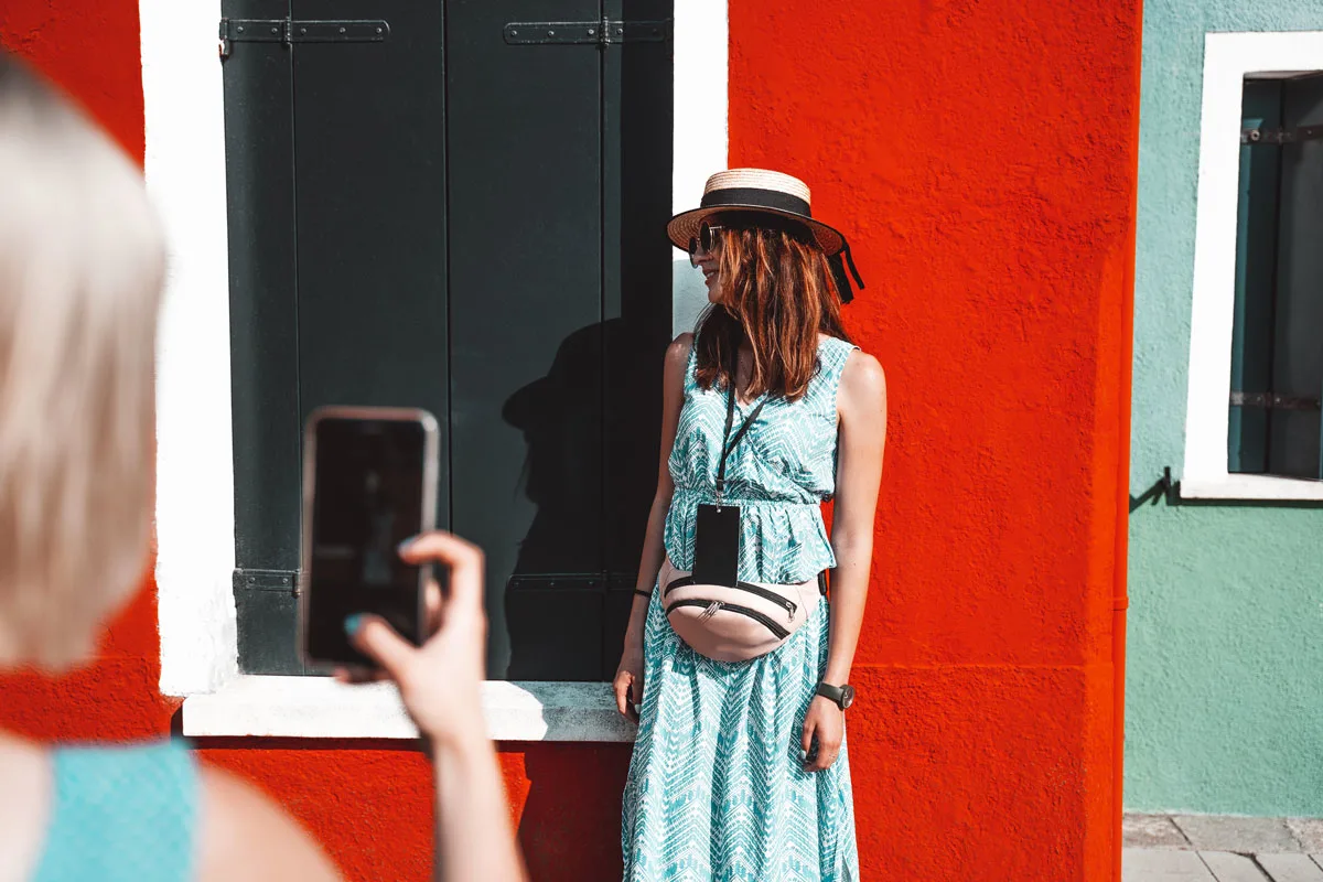 A young girl wearing a stylish fanny pack for travel being photographed against a bright orange wall.