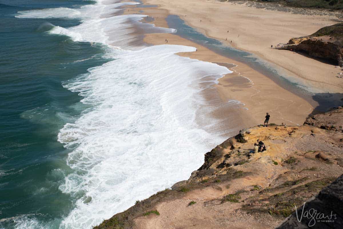 Men standing on cliffs over the big waves of Nazaré in Portugal. 