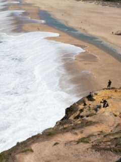 Men standing on cliffs over the big waves of Nazaré in Portugal.