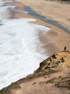Men standing on cliffs over the big waves of Nazaré in Portugal.