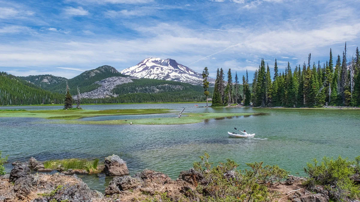 Man kayaking in a clear lake with snow capped mountains in the distance in Bend Oregon.