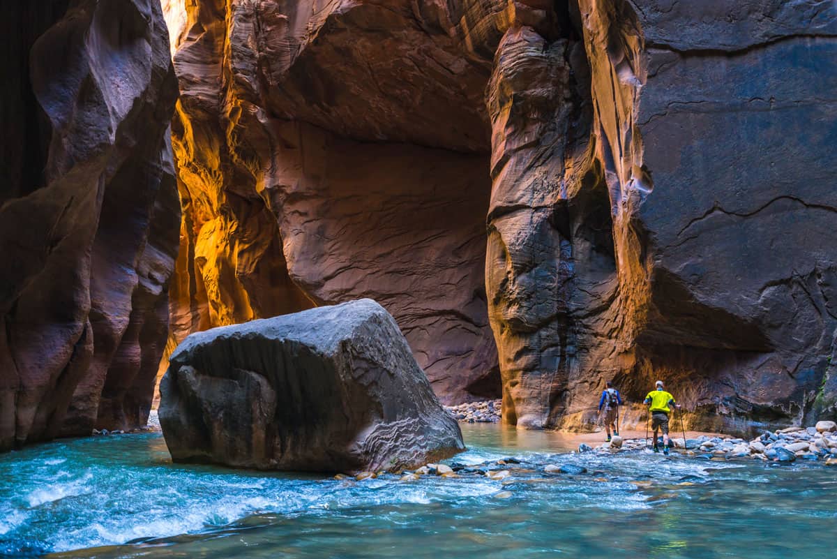 Two hikers walking through shallow water in a gorge in Zion National park.