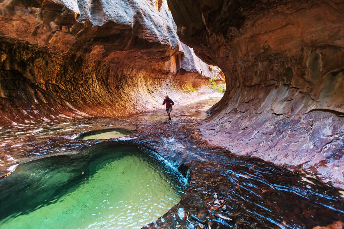 Hiker walking through shallow water in a canyon in Zion National Park. 
