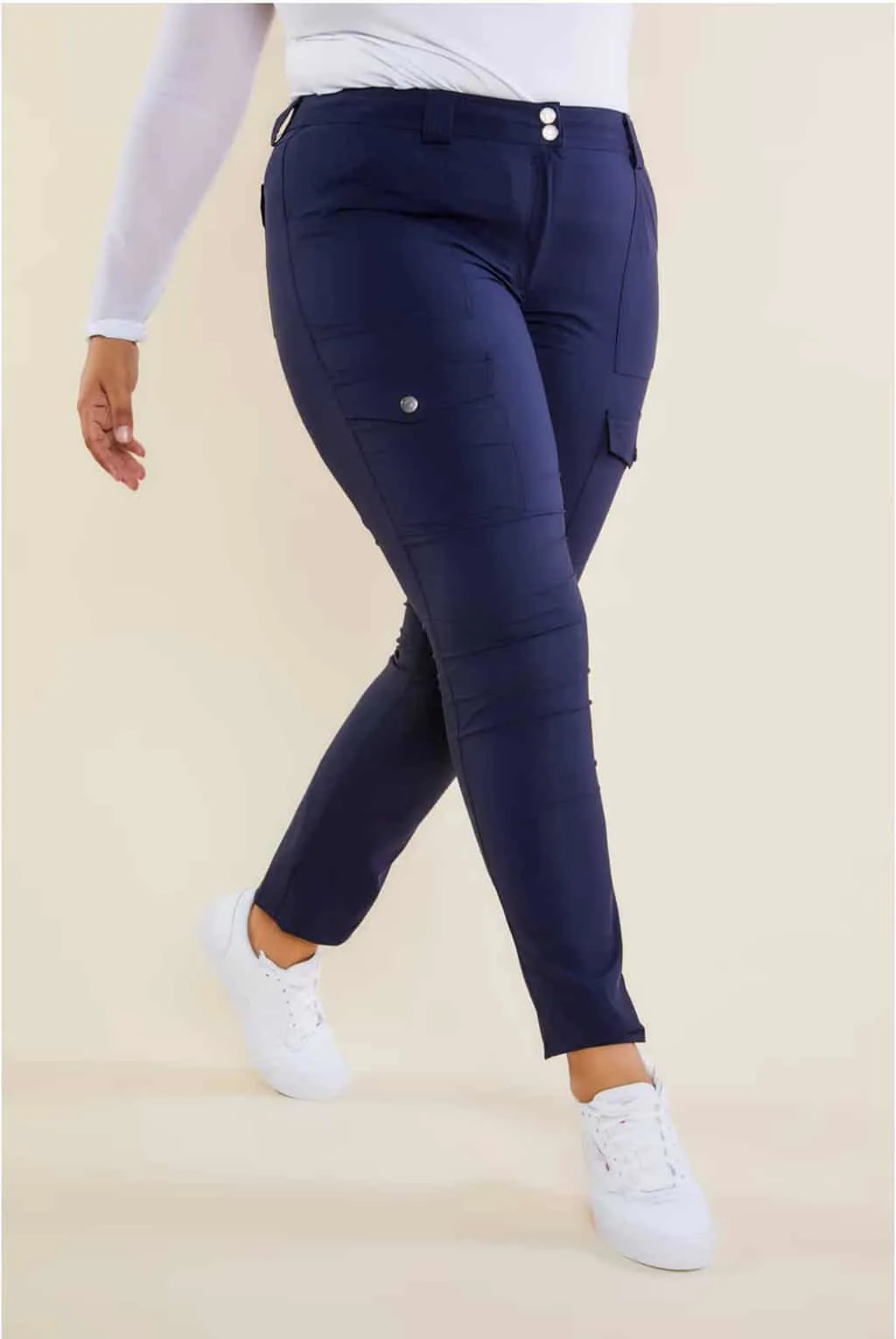 Woman modelling waist down navy travel pants with white top and white sneakers.