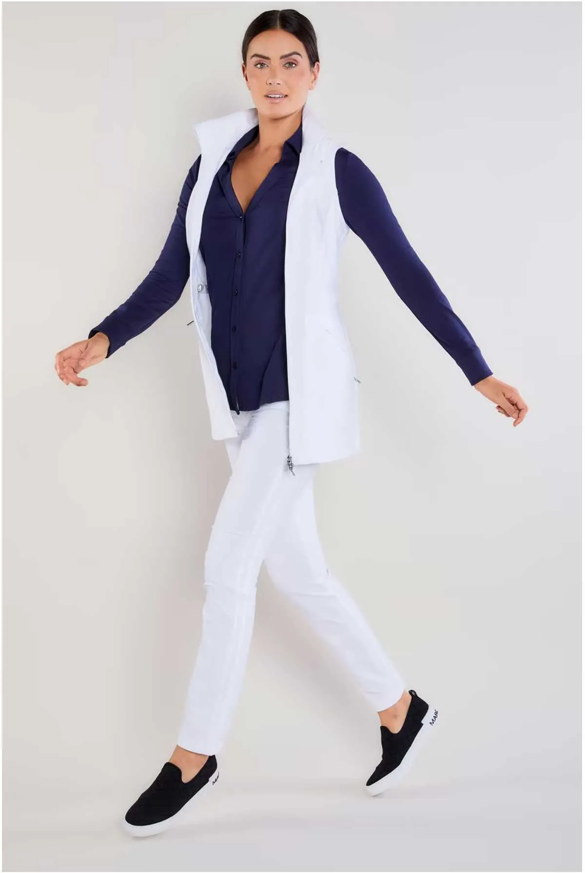 Lady modelling a pair of white travel pants with a blue shirt and whit vest jacket. 