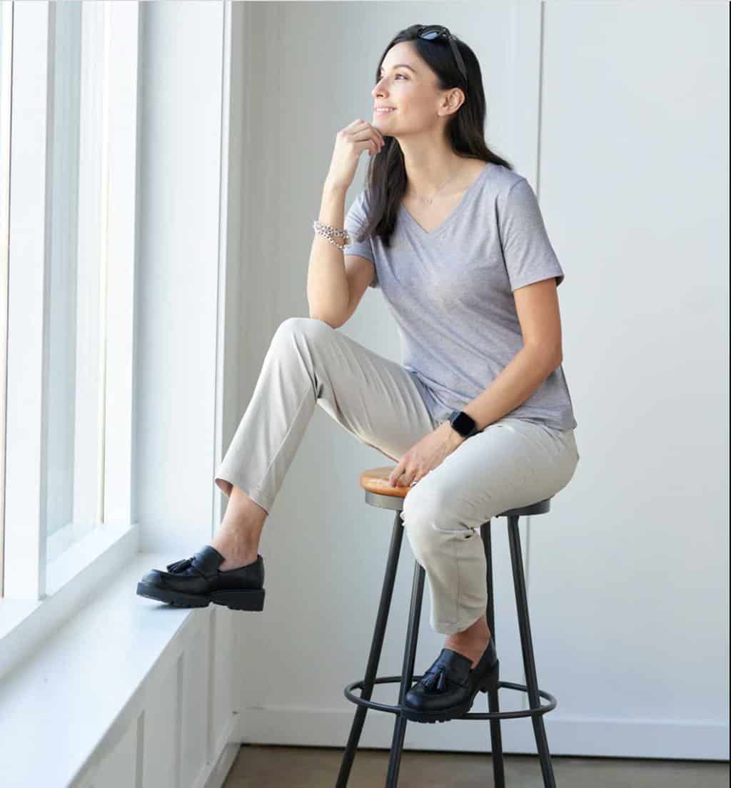 Woman sitting on a stool modelling a pair of beige women's travel pants with a grey T-shirt.  