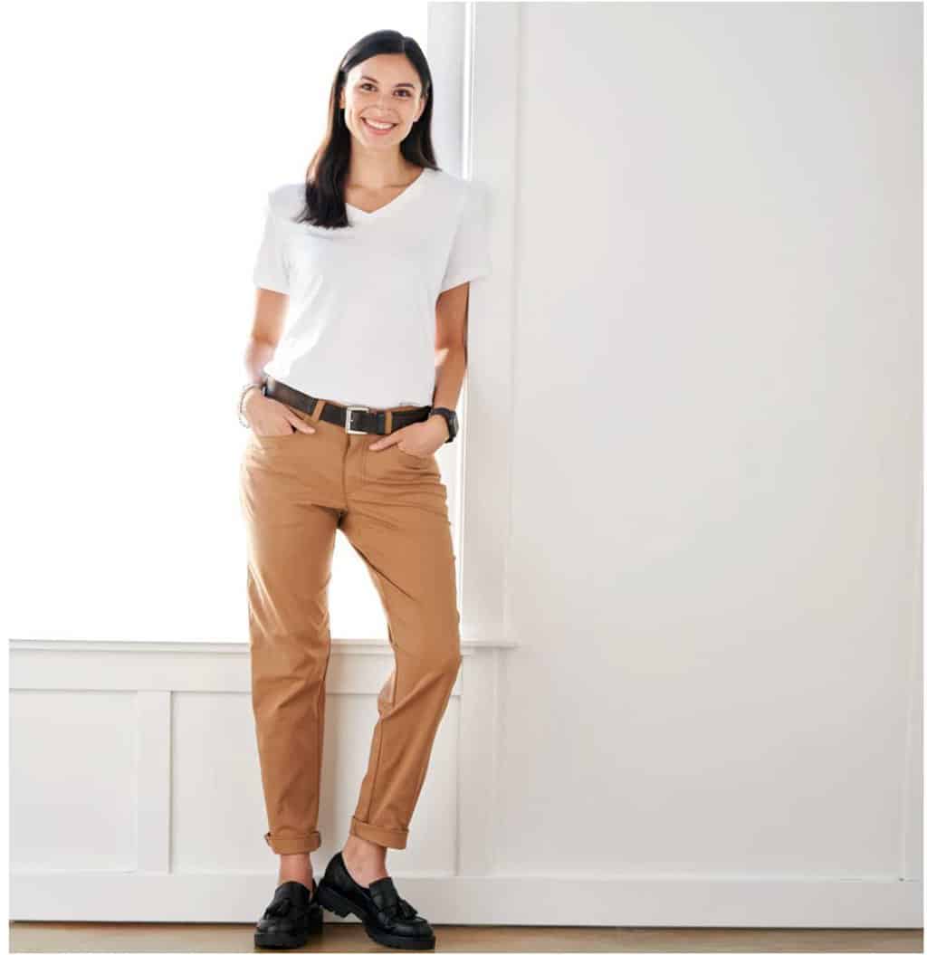 Lady in a white Tshirt next to a window modelling a pair of tan travel pants. 