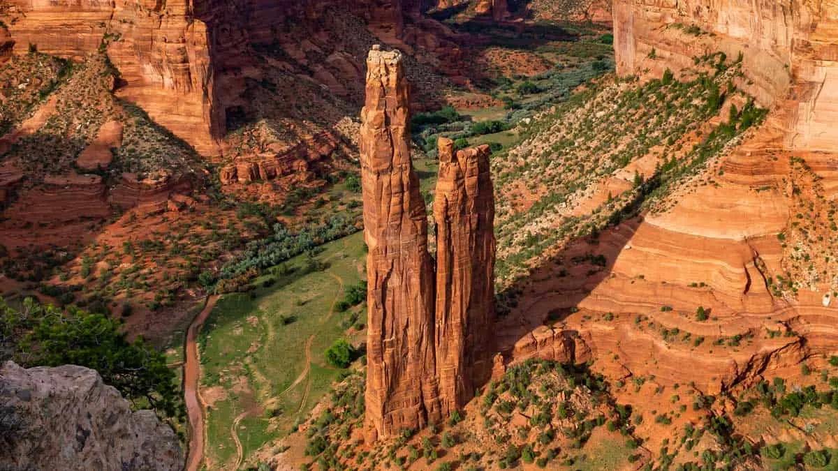 Red canyon with green valley and tall rock spire in Canyon De Chelly.