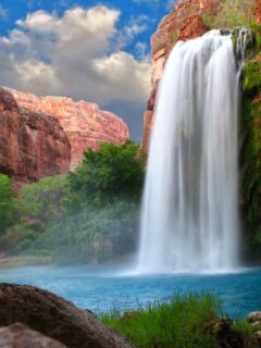 Waterfall into a blue swimming hole surrounded by red sandstone cliffs in Arizona desert.