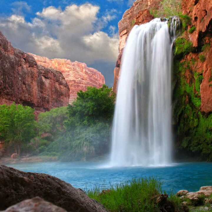 Waterfall into a blue swimming hole surrounded by red sandstone cliffs in Arizona desert.