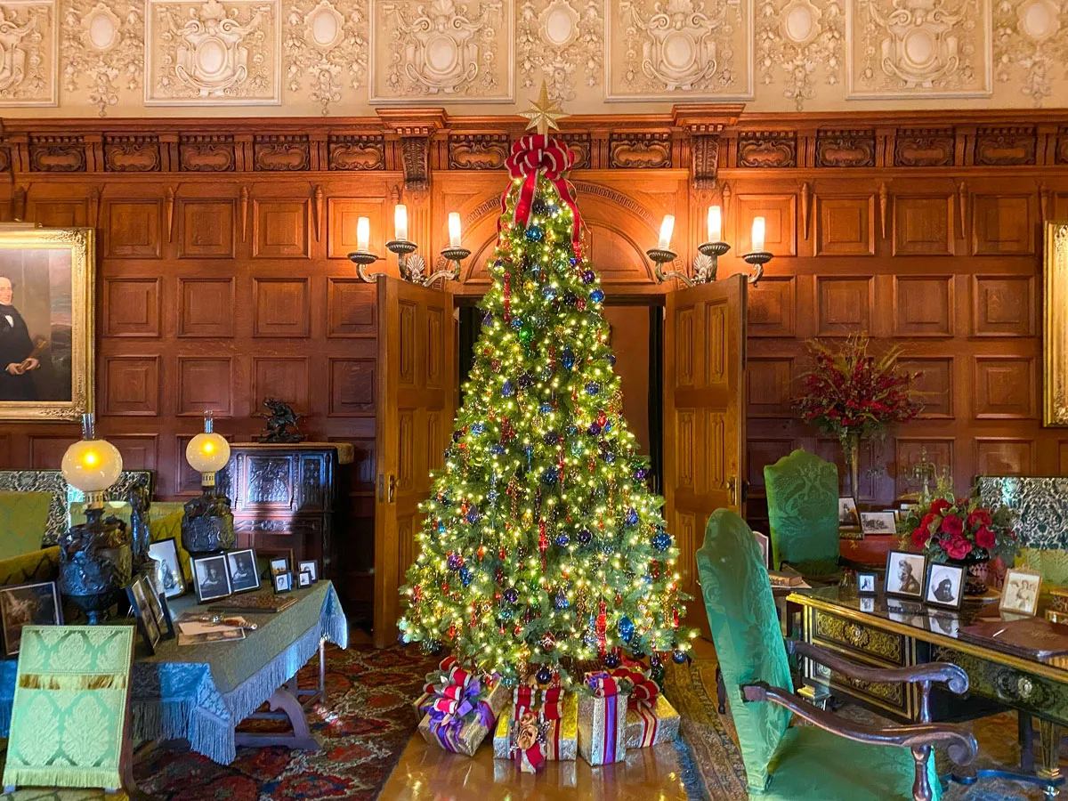 A large Christmas tree in an elegant wood panelled room. 