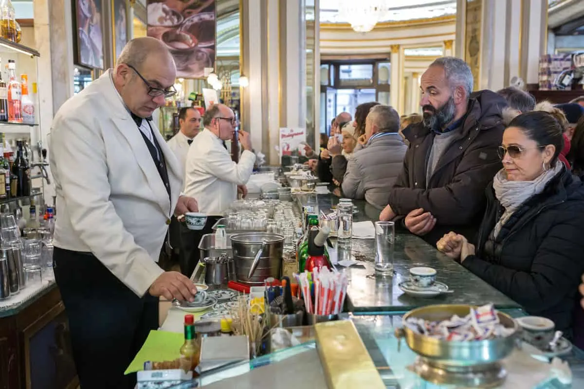 A man and a woman drinking coffee at the bar in the crowded famous Italian Cafe Gambrinus in Naples. The waiers wear traditional white coats. 