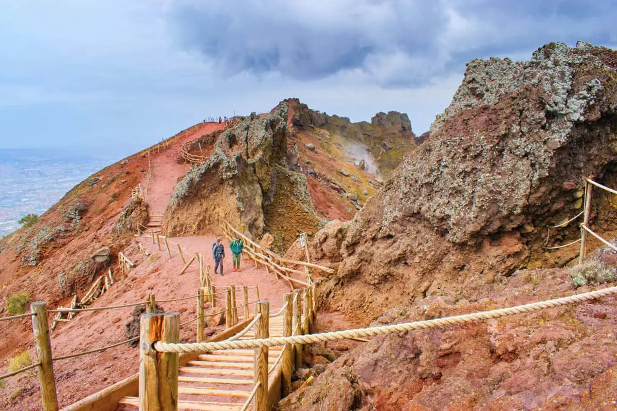 Two men walking along the red dirt trail that traces the rim of the Mt Vesuvius crater. 