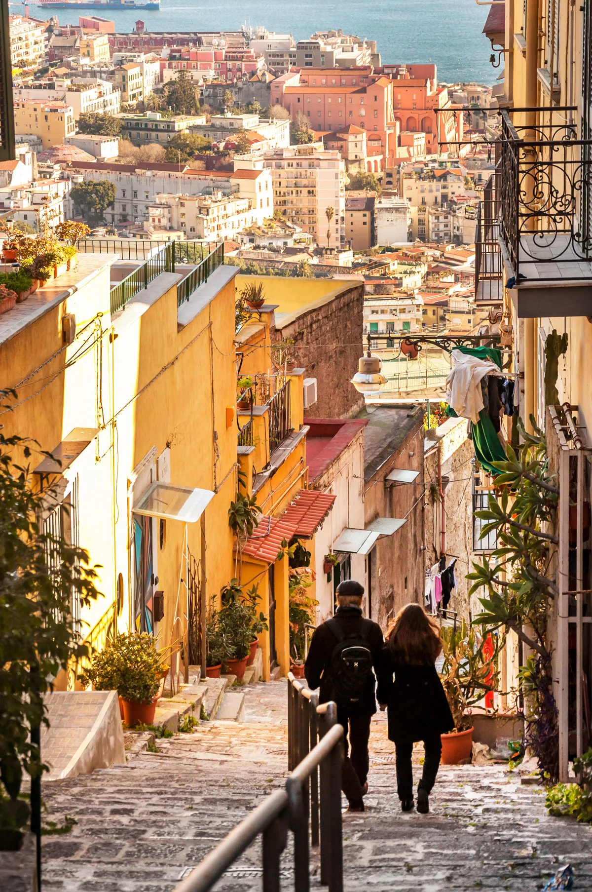 Young couple walking down hill on a narrow street overlooking the city of Naples in Italy. 