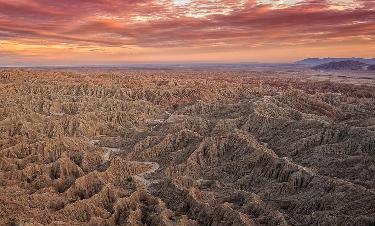 Wave like rock formations sprawl out across the desaert landscape of Borrego State park at sunset giving the entire scene a pink hue.