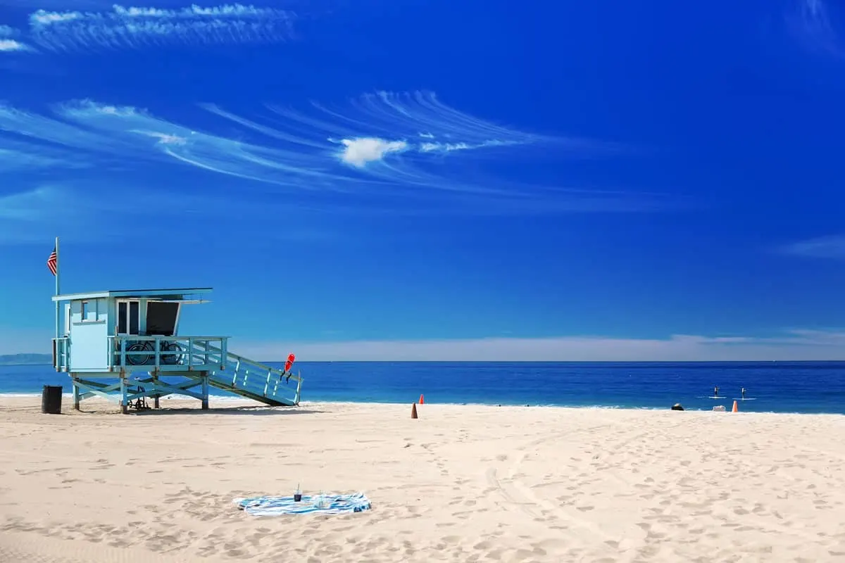 A pale blue life guard station on Hermosa Beach in South Bay LA. The beach is empty beach with very white sand and blue water on a clear day. 