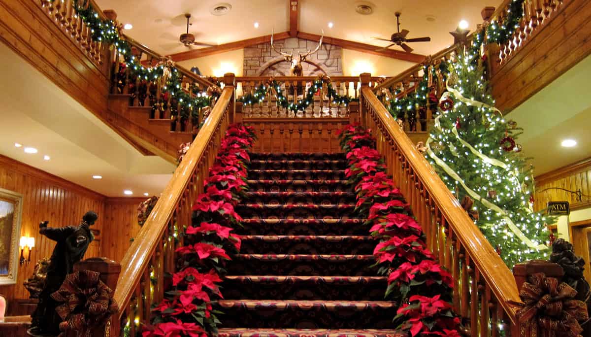 Poinsettias decorating a grand wooden stair case in a hotel with a giant Christmas tree next to the stairs.  
