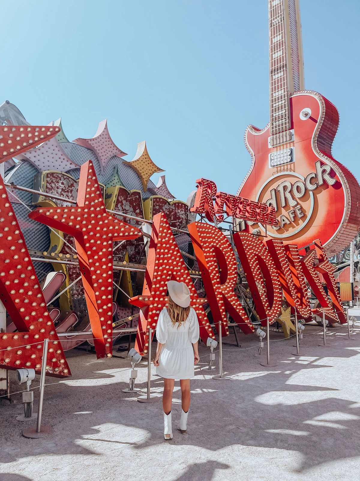 Girl in a white dress and cowboy hat standing in front of red signs and a giant Hard Rock Guitar in Las Vegas. 