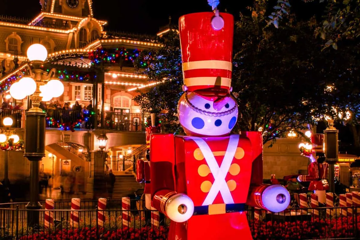 Nutcracker toy soldier in front of a building a Disneyland covered in Christmas lights at night. 