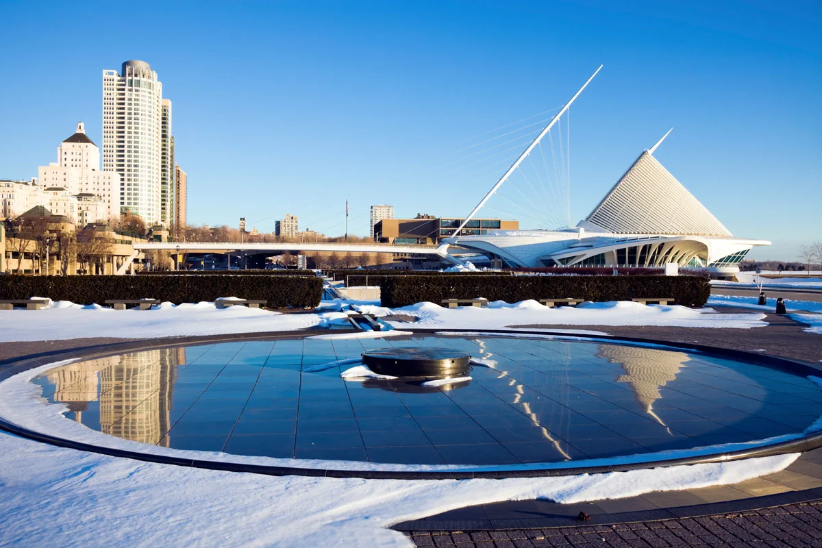 City skyline views of Milwaukee ona sunny day with snow on the ground and building reflecting in a pond. 